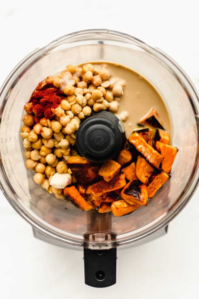 a food processor with sweet potato, tahini, chickpeas, garlic and paprika in it