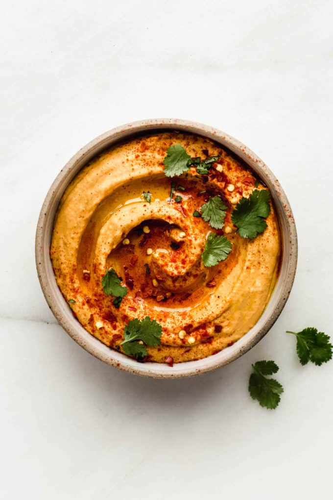 A bowl of hummus flavoured with sweet potato topped with cilantro leaves