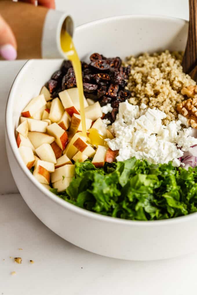 salad dressing being poured into a bowl of apple quinoa salad